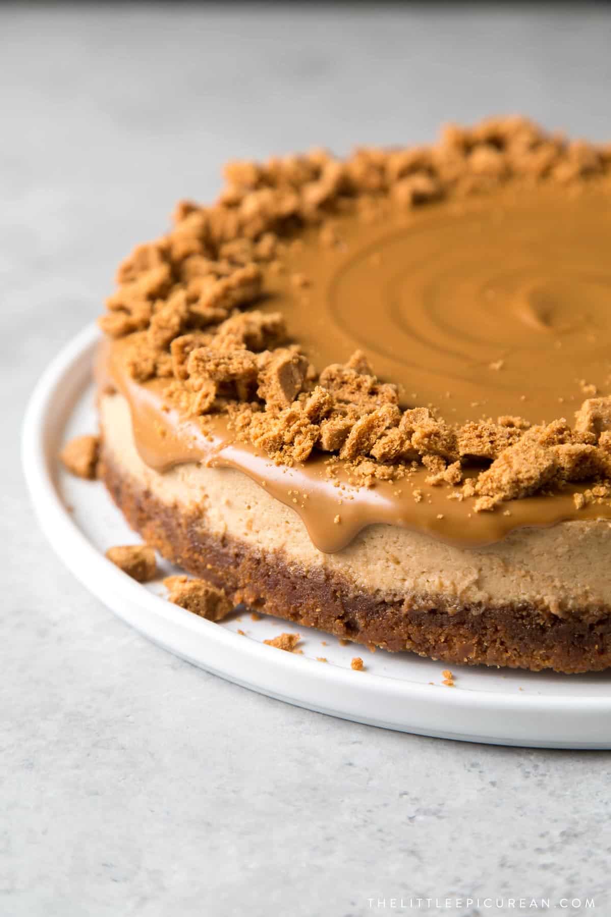 biscoff cheesecake topped with melted cookie butter and garnished with crushed biscoff cookies on white serving platter.