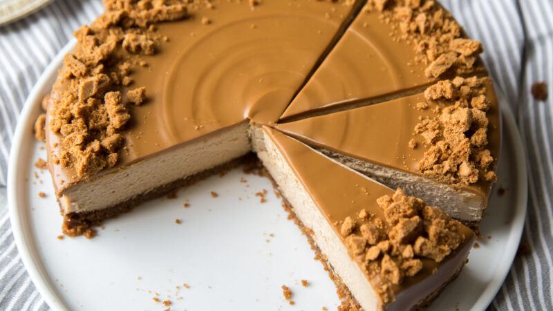 biscoff cheesecake topped with cookie butter spread and chopped cookies sliced into portions.