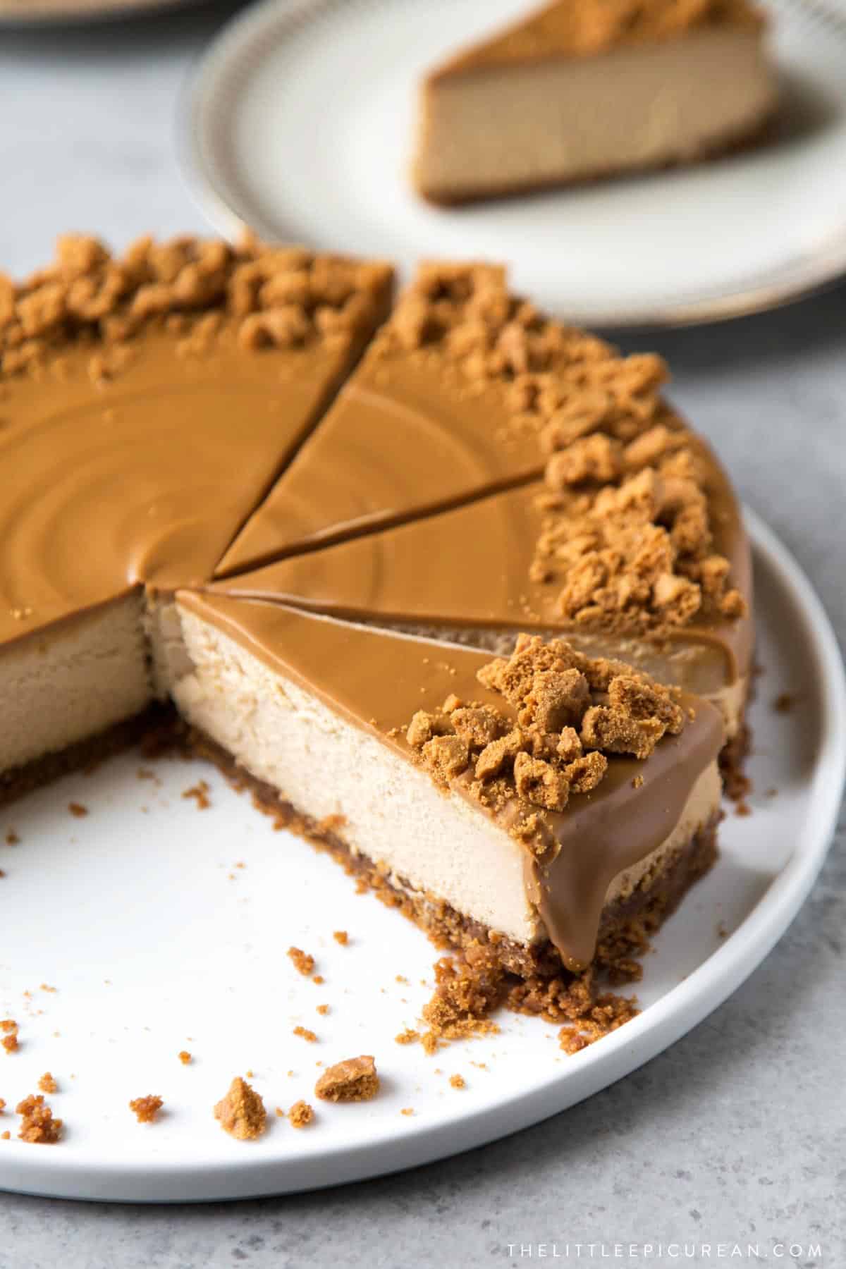 cookie butter topped biscoff cheesecake slice with crumbled cookie bits on white serving plate.