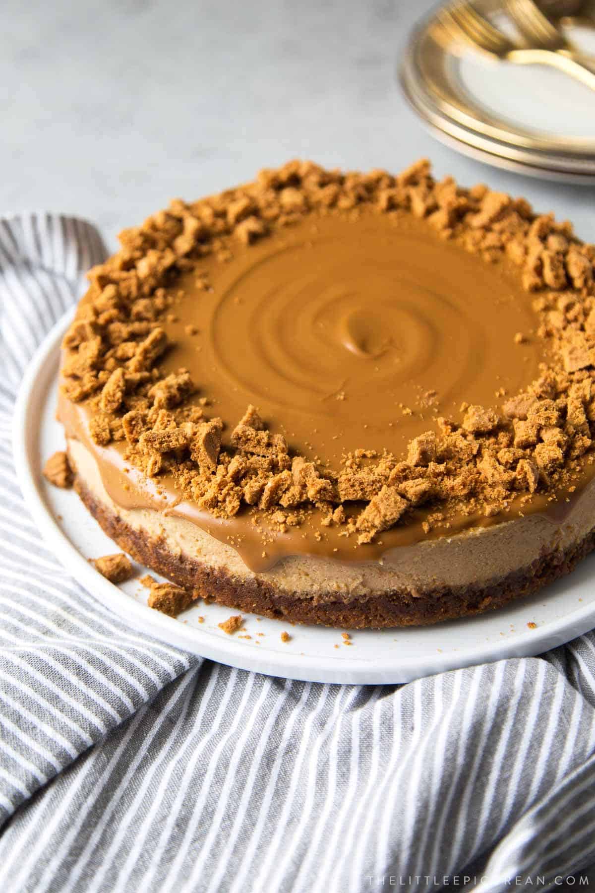 biscoff cheesecake on white serving platter on top of striped linen.