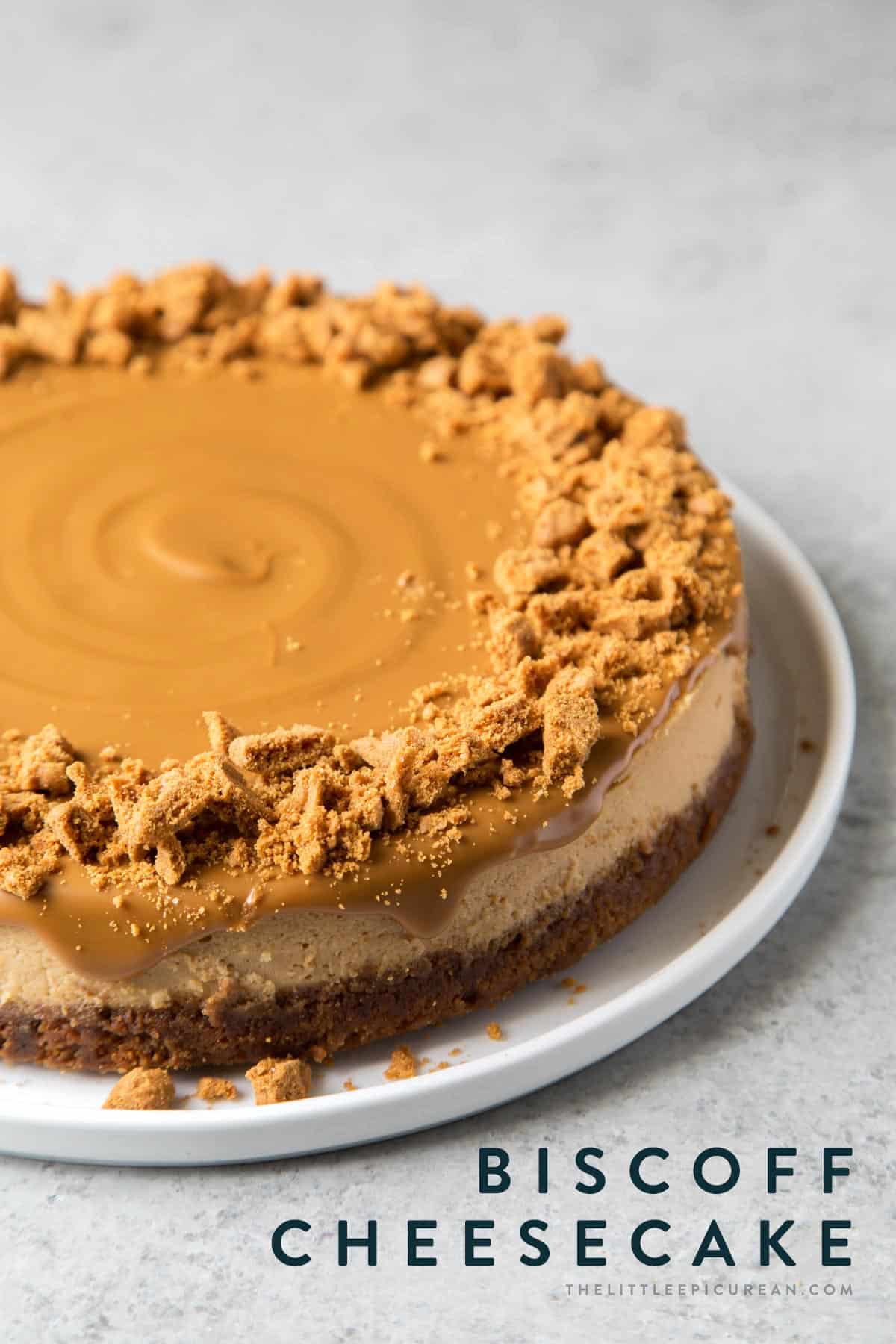 biscoff cheesecake topped with melted cookie butter spread and garnished with crushed biscoff cookies on white serving plate.