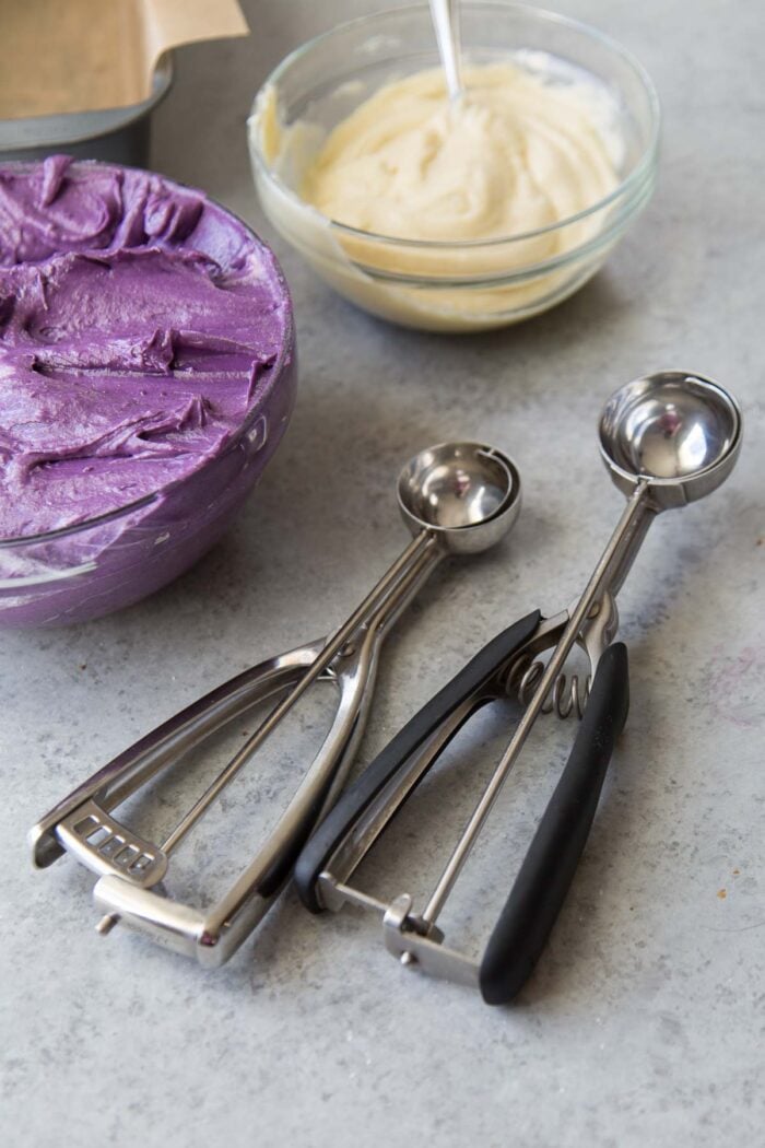 use cookie scoop to distribute ube and vanilla cake batter into loaf pans.