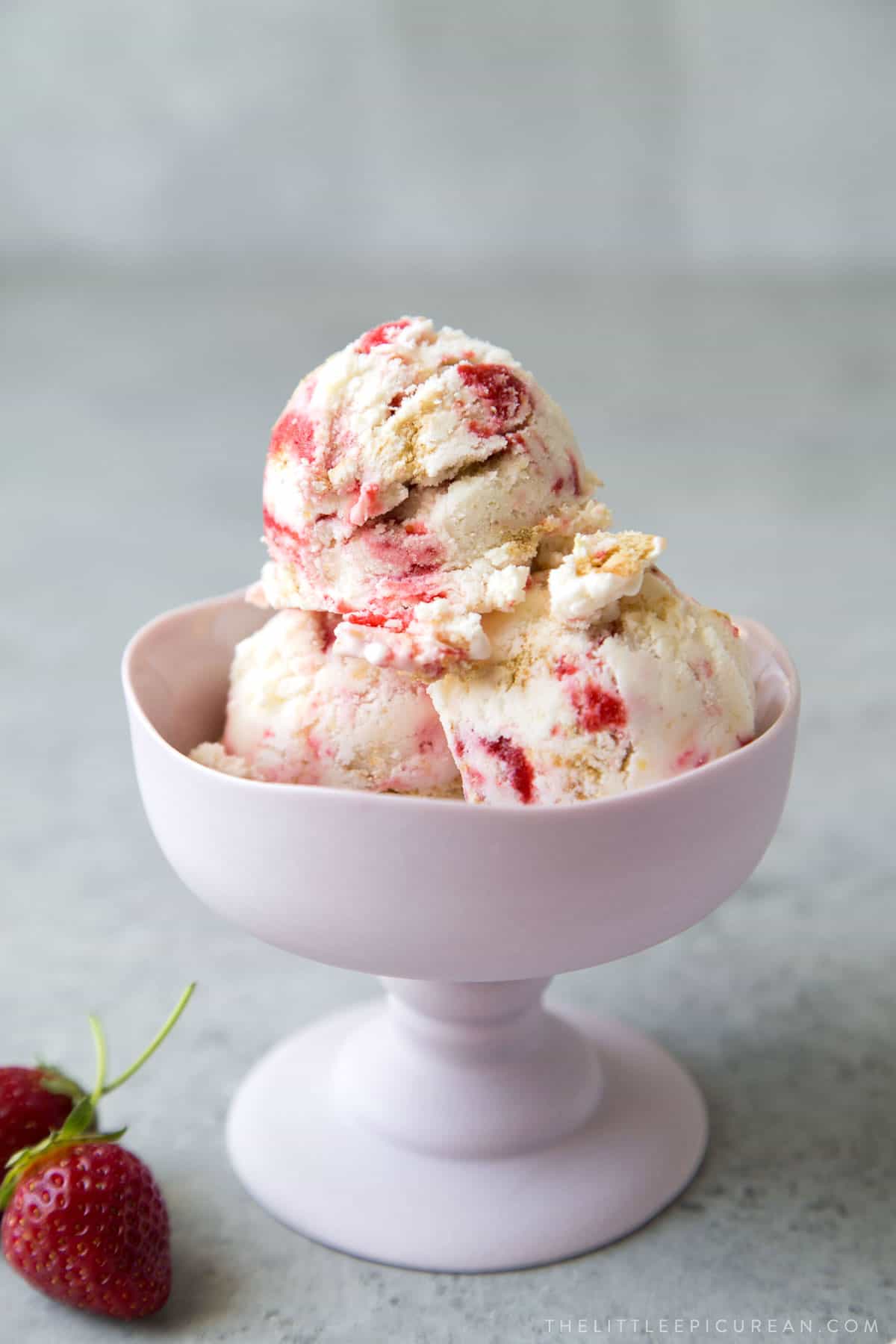 strawberry cheesecake ice cream scoops served in stemmed ice cream dish.