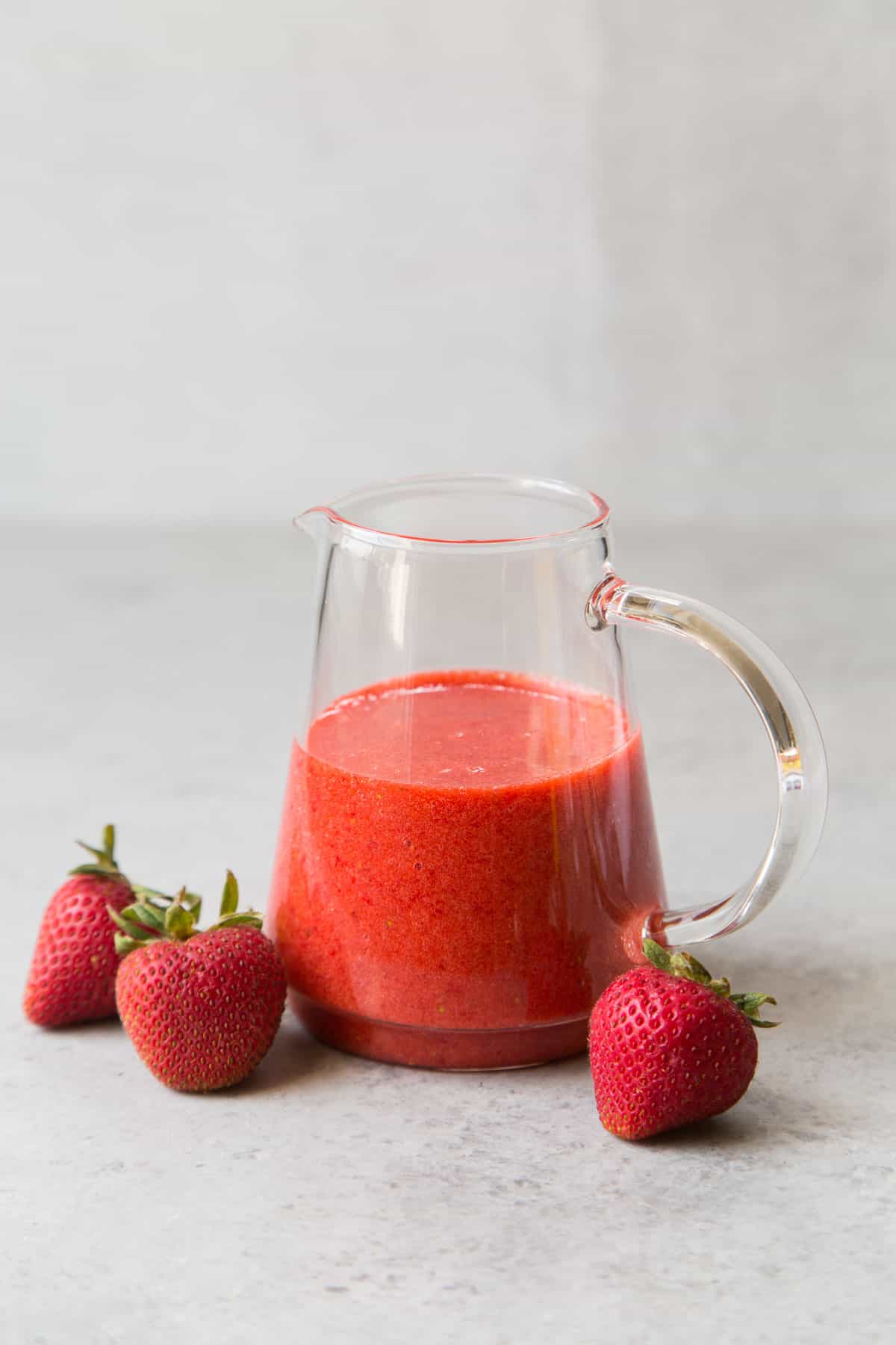 vibrant red fresh strawberry sauce in small pitcher.