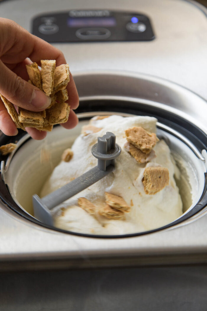adding chopped graham crackers to cheesecake ice cream.