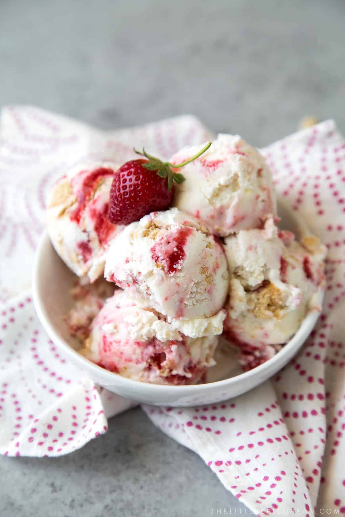 several scoops of strawberry cheesecake ice cream in a bowl with fresh strawberry.