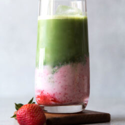 layered strawberry milk and matcha in a tall serving glass served with fresh strawberry.