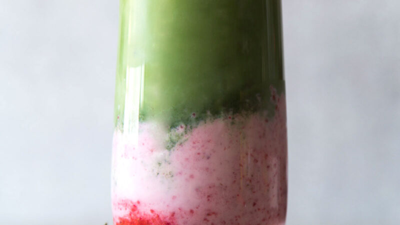 layered strawberry milk and matcha in a tall serving glass served with fresh strawberry.