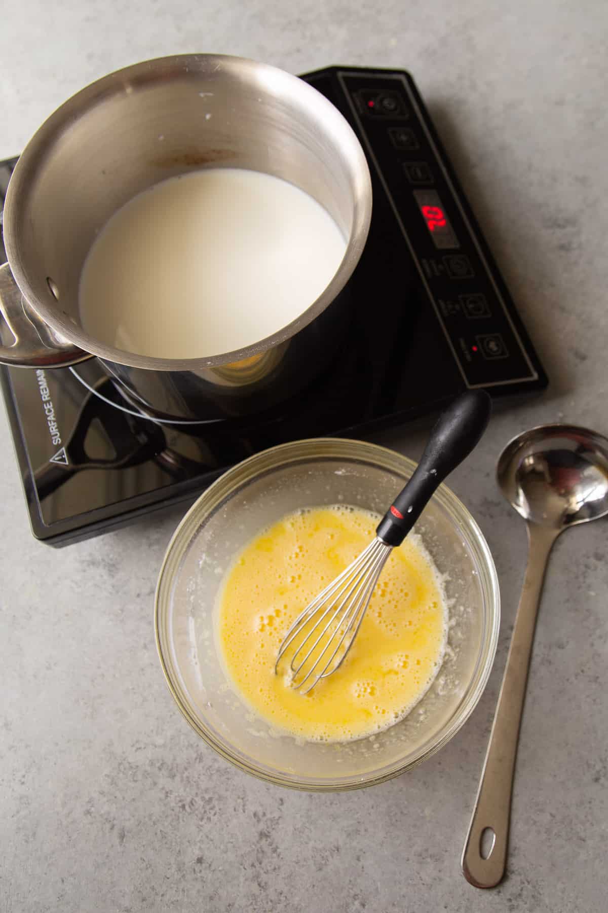 pastry cream set up with induction burner, pot, egg mixture, and ladle.
