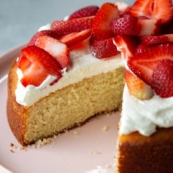 slice taken out of almond cake topped with whipped cream and sliced strawberries.