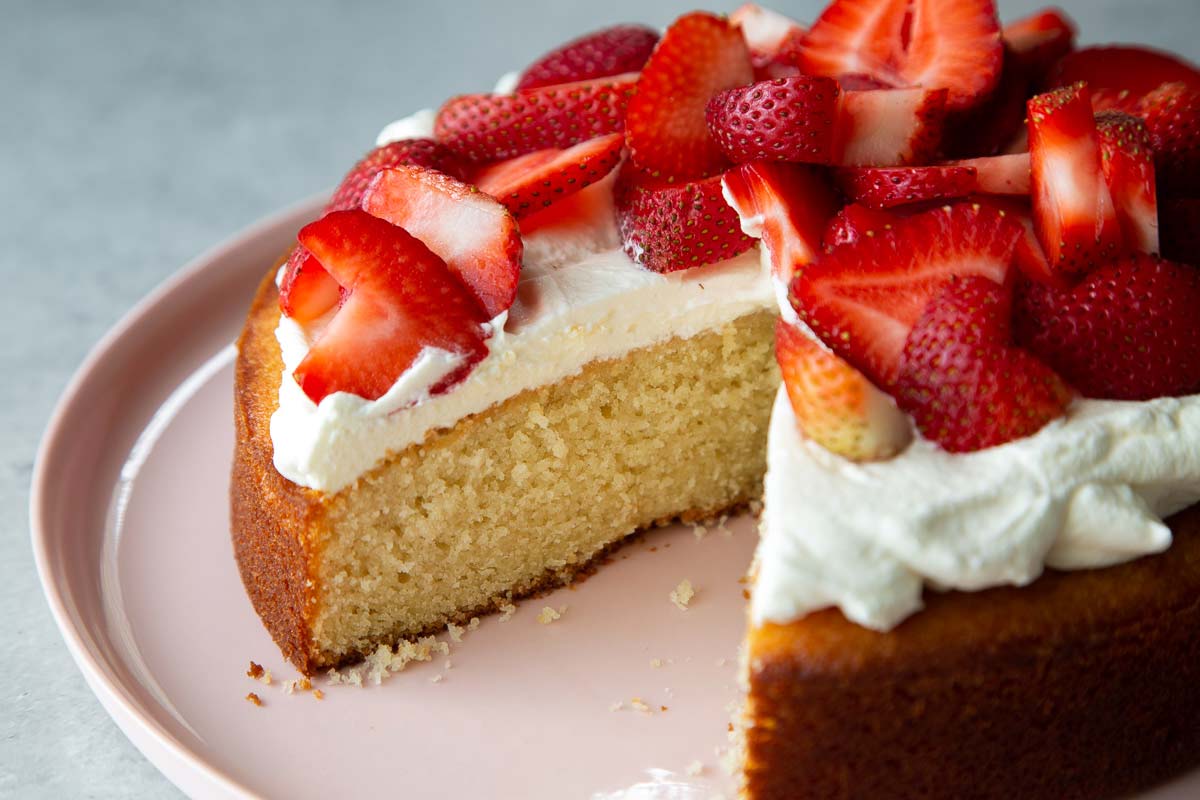 slice taken out of almond cake topped with whipped cream and sliced strawberries.