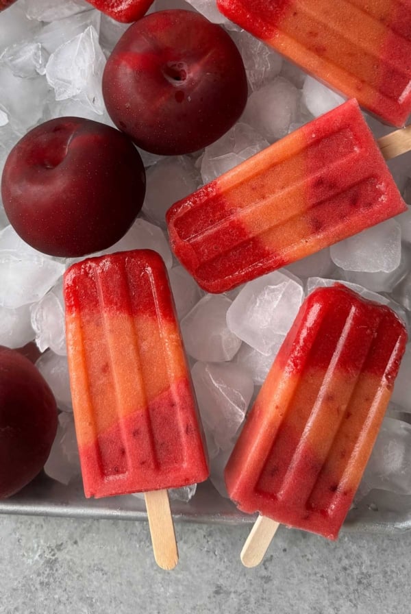 layered summer fruit popsicles on ice lined sheet tray.