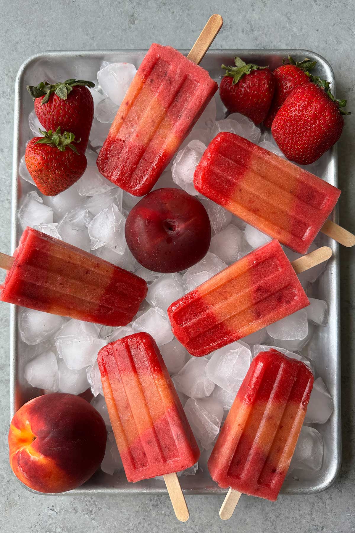 layered summer fruit popsicles on ice lined sheet tray.