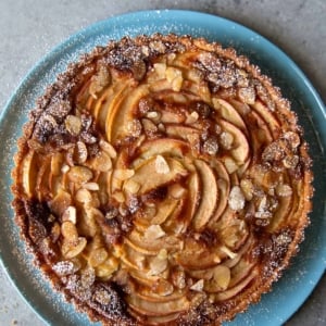 overhead of apple frangipane tart dusted with powdered sugar on blue serving plate.