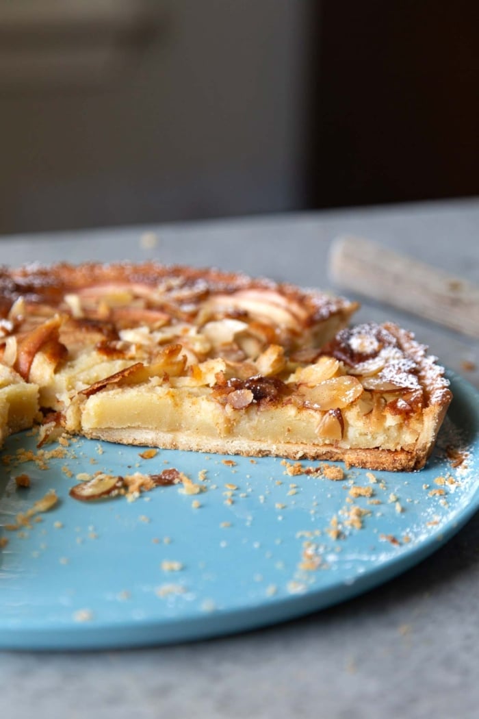 slice of apple frangipane tart shows the distinct layers of crust and filling.