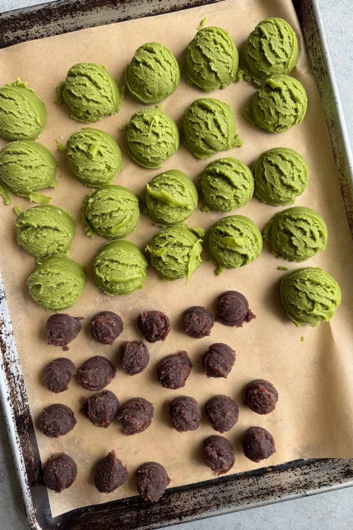 scoops of matcha cookie dough and scoop of red bean paste arranged on parchment lined baking sheet.