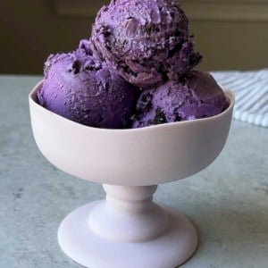 three scoops of ube cookies and cream ice cream in stemmed glass.