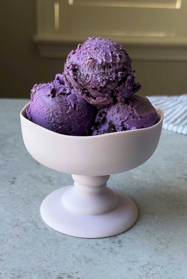 three scoops of ube cookies and cream ice cream in stemmed glass.