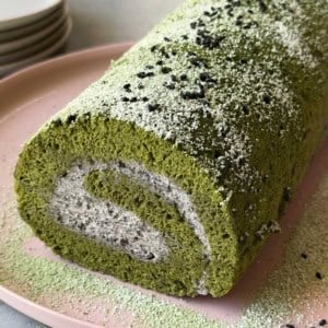 close up of matcha Swiss roll cake filled with black sesame mousse on pink seeing plate.