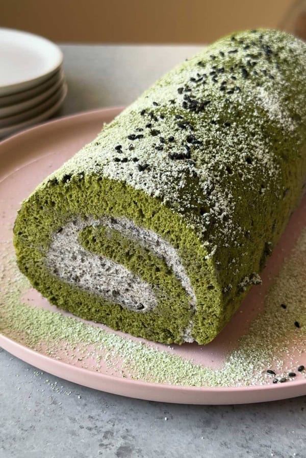 matcha Swiss roll cake filled with black sesame mousse on pink seeing plate.