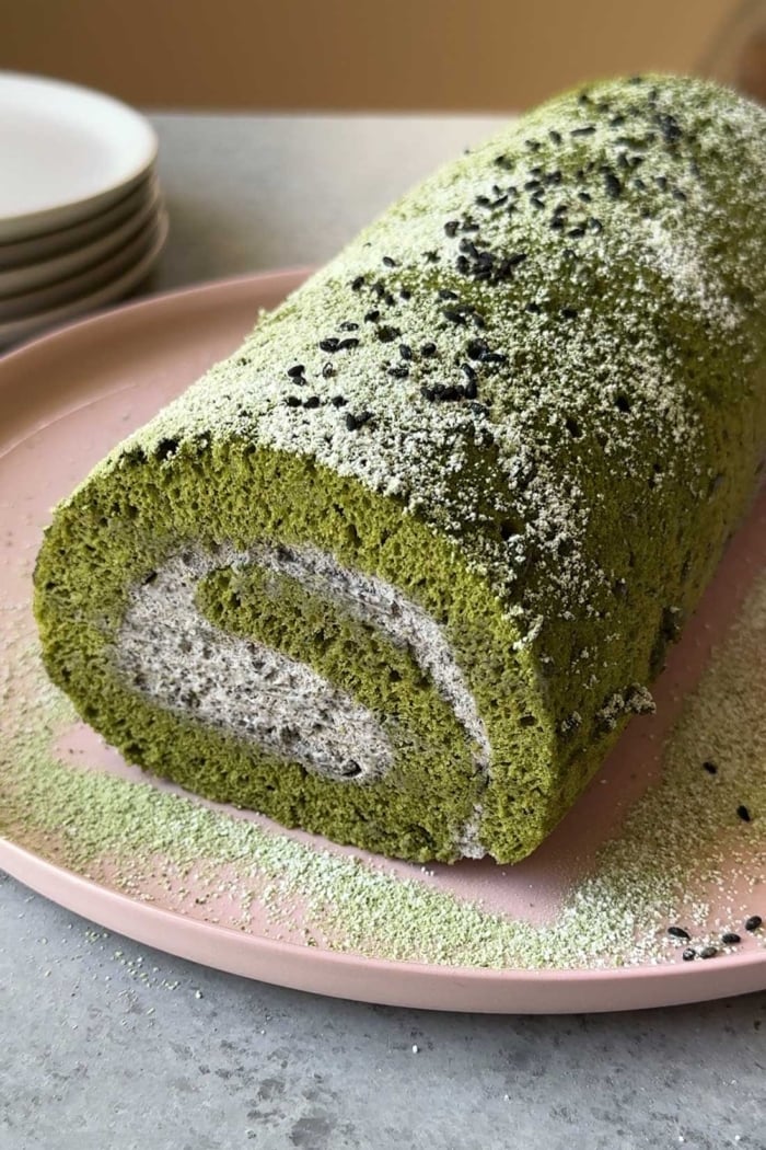 matcha Swiss roll cake filled with black sesame mousse on pink seeing plate.