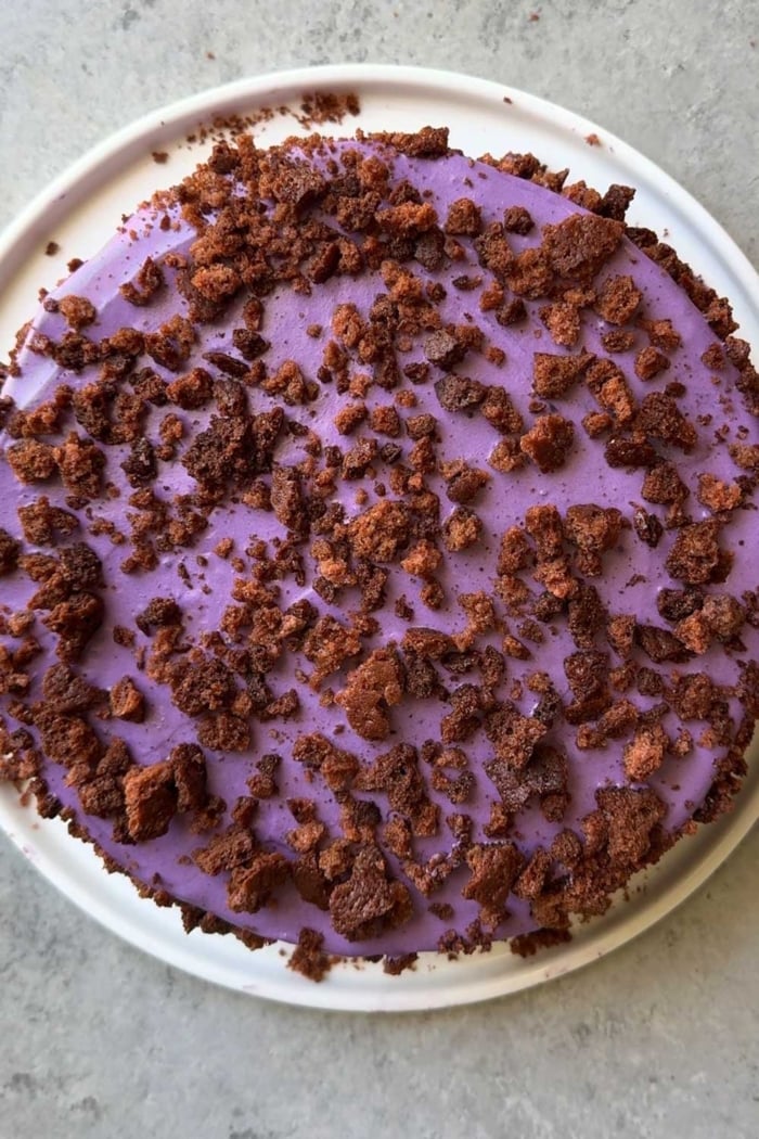 overhead of ube layer cake garnished with ube cake crumbs on white serving plate.