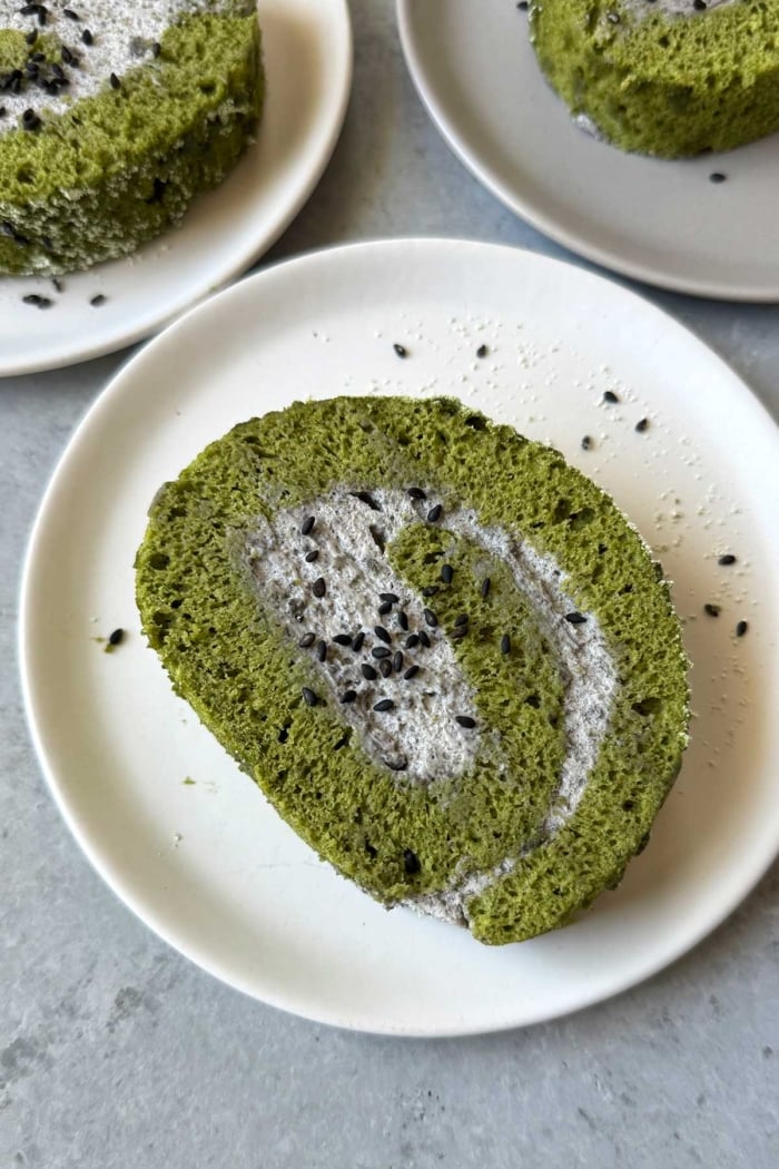 close up slice matcha roll cake with black sesame mousse filling on white plate.