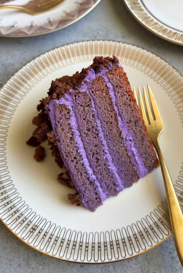 slice of sour cream ube layer cake on serving plate with gold cake fork.