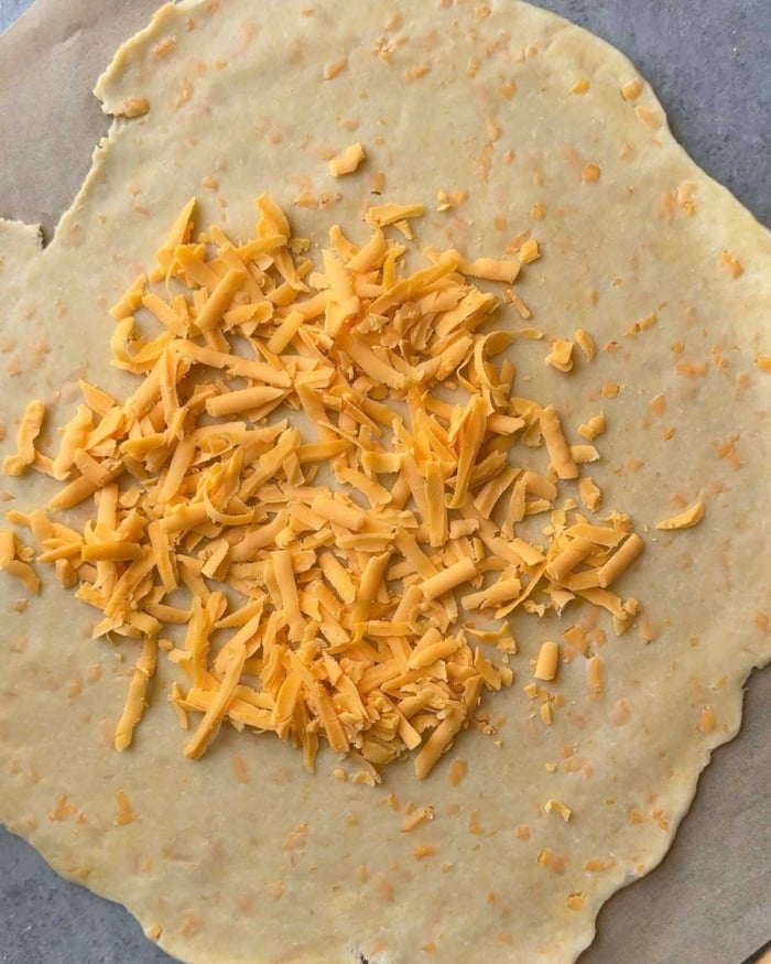 rolled out dough topped with shredded cheddar cheese.