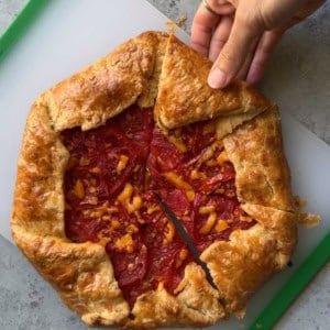 sliced cheddar tomato galette on cutting board with hand pulling out one slice.