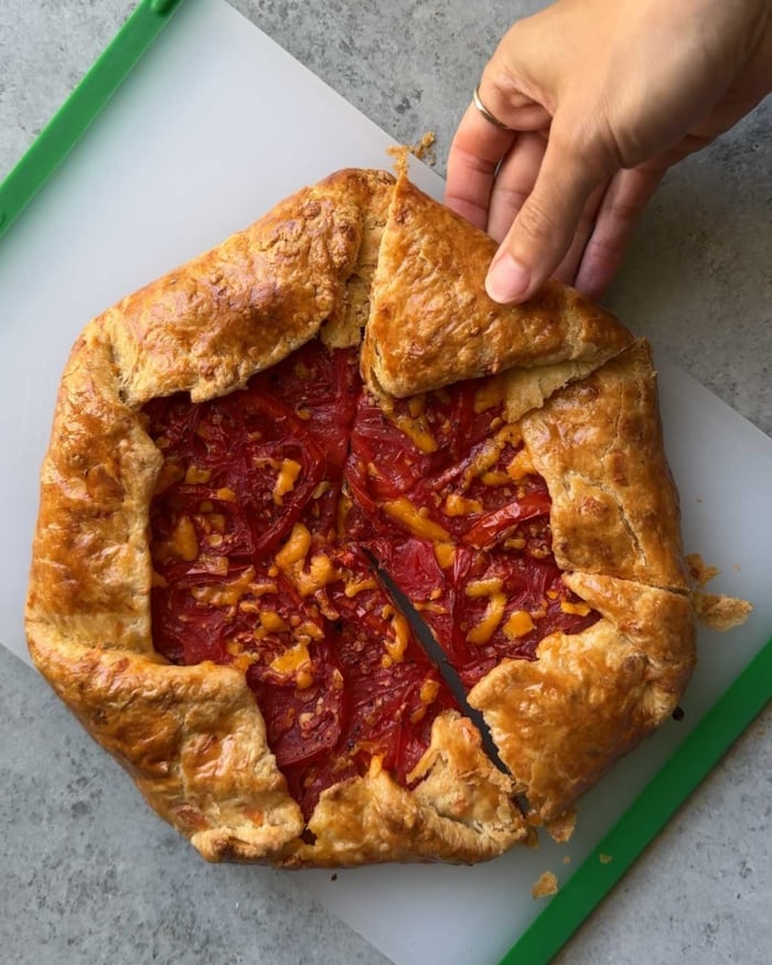 sliced cheddar tomato galette on cutting board with hand pulling out one slice.