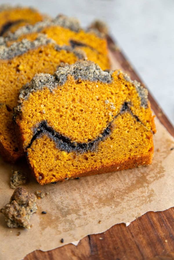 pumpkin loaf cake with black sesame crumble on parchment paper lined wooden board.