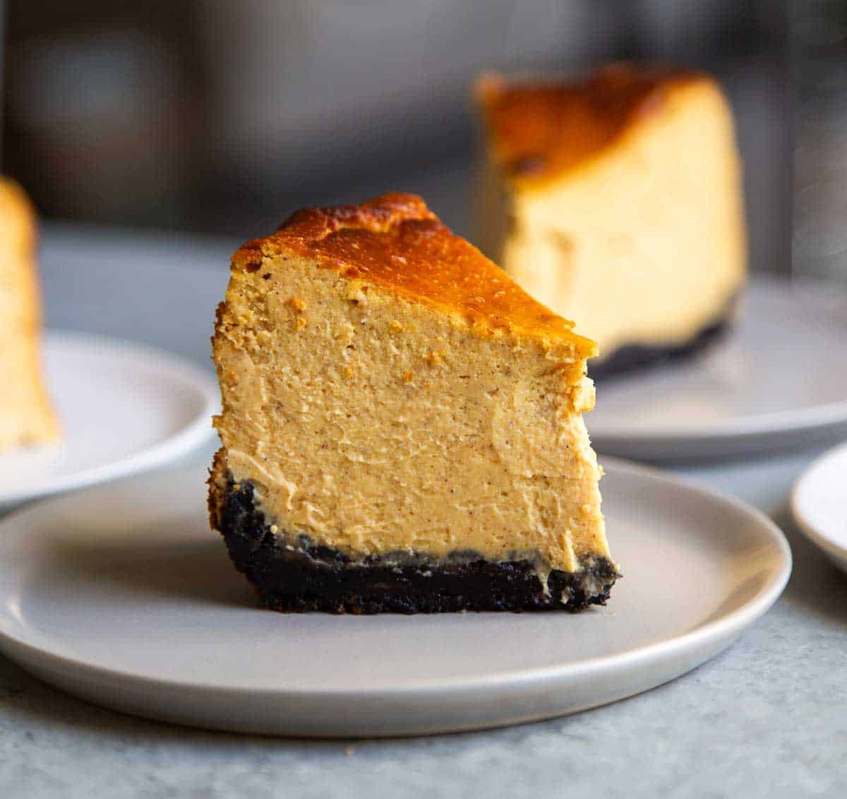 slice of oreo crust pumpkin Basque cheesecake on grey plate.
