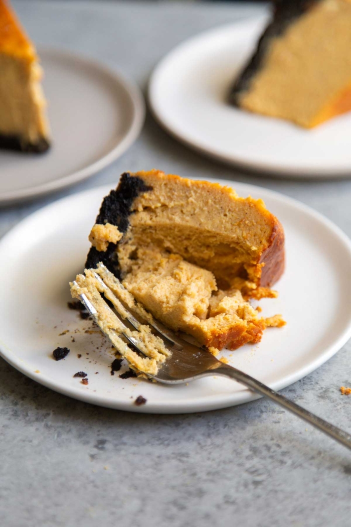 fork sliced through pumpkin Basque cheesecake on white plate.